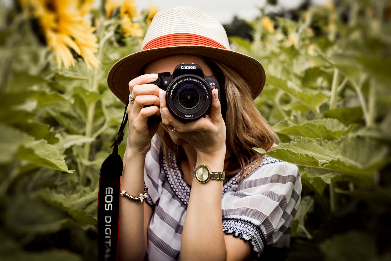 Services Woman with hat photographing sunflowers in a summer field using a Canon camera.